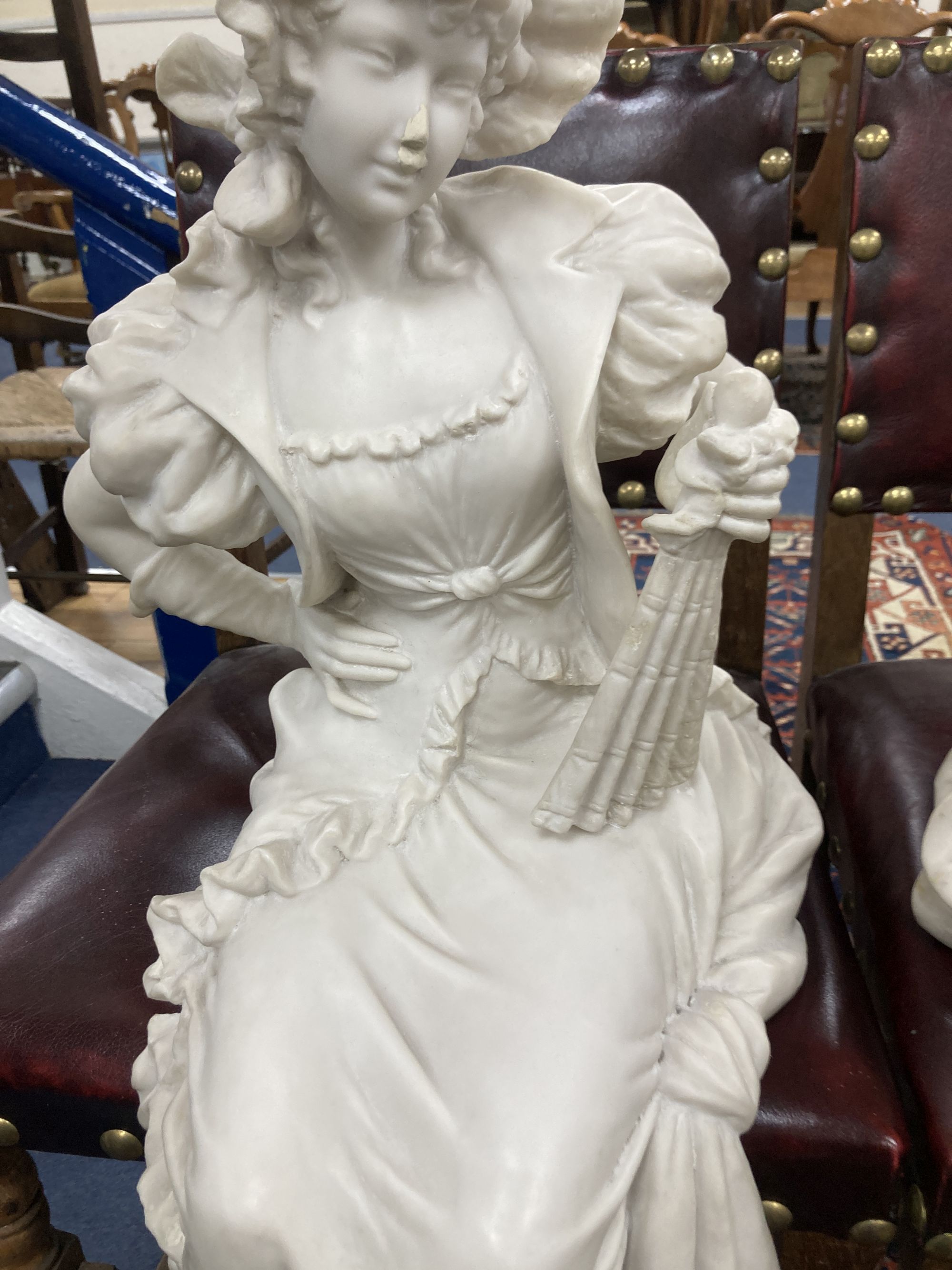 A pair of resin marble seated figures of a Dandy and a Dandizette on ebonised plinths